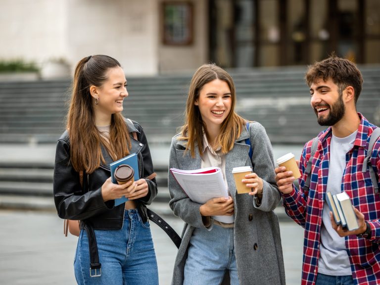Two female and one male university student enjoying coffee and carrying papers