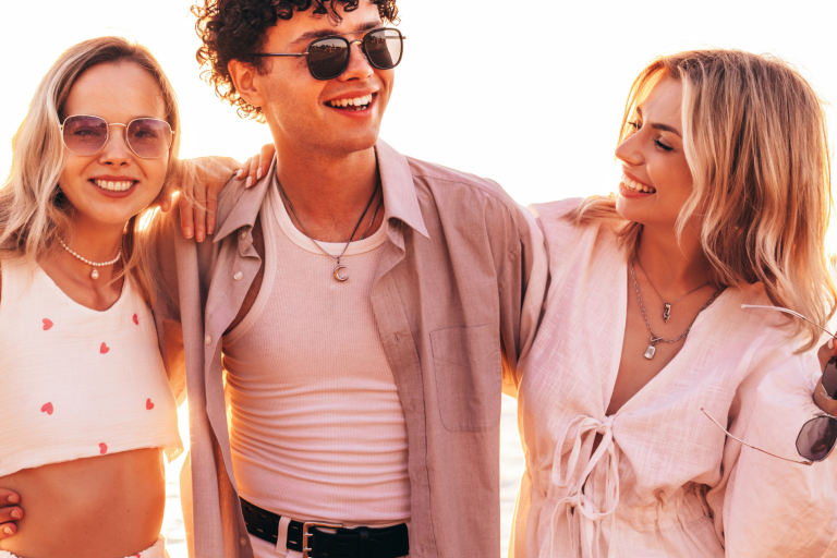 A young man and two young women in light clothes on the beach